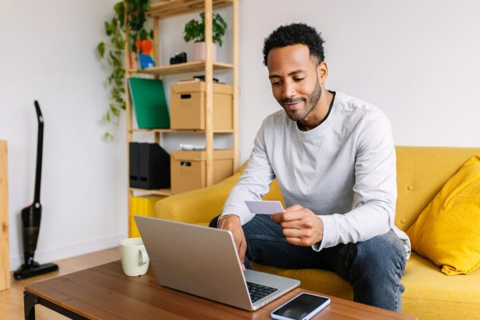 Person-holding-credit-card-at-home-while-using-laptop-in-living-room_Xavier-Lorenzo.jpg